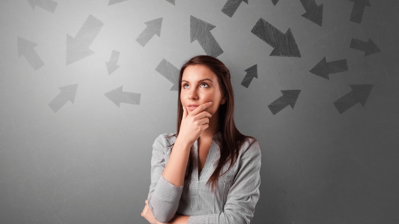 Thoughtful young woman making a decision with arrows pointing in different directions on a gray background