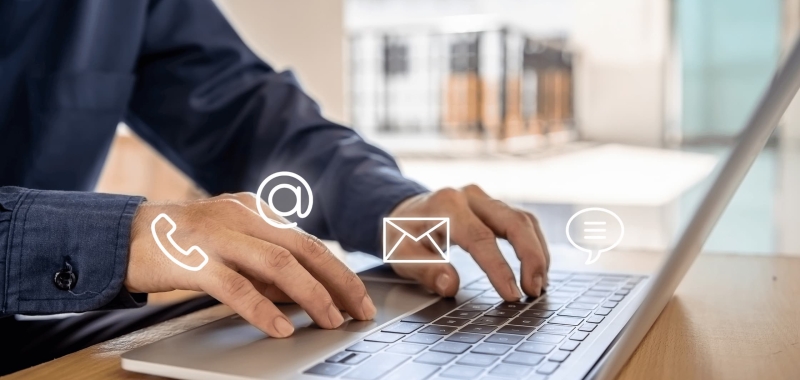Close-up of hands typing on laptop keyboard with digital contact icons for phone, email, and messaging