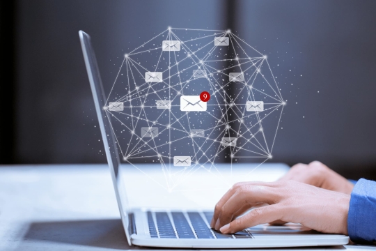 Hands typing on a laptop with digital email icons and network connections, representing online communication